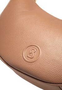 Camelkleurige leren crossbodytas met een gestructureerd oppervlak en een cirkelvormig logo dat op de voorkant is geperst. Voorzien van een goudkleurig metalen accent.