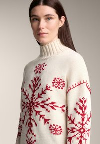 Strickpullover in Creme mit hohem, geripptem Kragen, verziert mit roten Schneeflockenmuster auf Brust und Ärmeln, gefertigt aus weichem Textilmaterial.