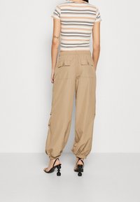 Beige cargobroek met elastische boorden, twee achterzakken met klep, gecombineerd met een gestreept kortermig shirt en zwarte sandalen met hak.