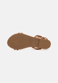 Vaaleanruskea sandaali, jossa on kuvioitu kumipohja, ohuet remmit ja metalliset yksityiskohdat. Malli on avoin varpaiden kohdalta ja mukavan muotoinen.