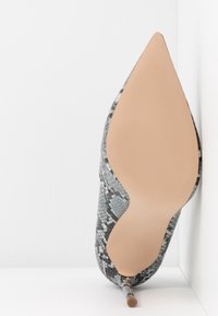 Chaussure à talon aiguille à bout pointu en imprimé serpent gris et noir, avec une semelle beige lisse et un talon stiletto fin.