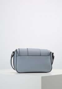 Blå läder crossbody-väska med en strukturerad form, texturerad yta, lockstängning och kontrasterande svarta sömmar vid kanterna.