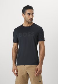 Sötétkék, rövid ujjú póló sima anyagból, diszkrét sötét logónyomattal és klasszikus kerek nyakkivágással.