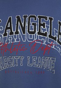Camiseta azul con texto en blanco y rojo: "LOS ANGELES Athletic Dept." y "VARSITY LEAGUE" con la fecha de establecimiento 1965 en texto más pequeño.