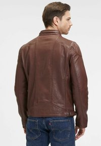 Giubbotto in pelle marrone con design a spalla rigata, dotato di bottoni a pressione in vita e taglio a misura. Dettagli di cucitura visibili in tutta la giacca.