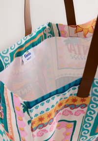 Tote bag avec des motifs géométriques et floraux colorés, des poignées en cuir marron et une étiquette Fanta Next près de l'ouverture avec une fermeture à bouton-pression.