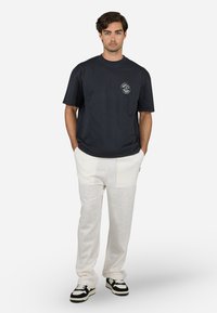 Tricou din bumbac de culoare albastru închis, cu guler rotund și mâneci scurte, având un mic logo alb. Asortat cu pantaloni din in ușori și de culoare deschisă.