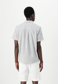 Camisa de manga corta en tejido ligero con rayas horizontales azules y blancas. La parte posterior cuenta con un canesú y un pliegue central. Combinada con pantalones cortos blancos.