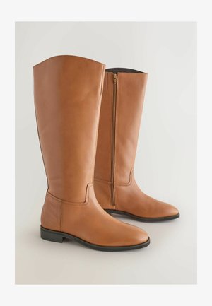 Botas de montar altas de cuero marrón con un diseño elegante, punta redondeada y un cierre lateral para ponerlas y quitarlas con facilidad. Suelas planas y mínimos detalles de costura.