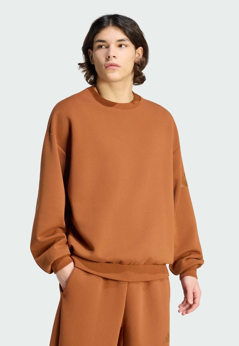 Braunes oversized Sweatshirt mit langen Ärmeln, geripptem Rundhalsausschnitt und Bündchen, weicher Textur, mit einem Logodetail auf der linken Seite.