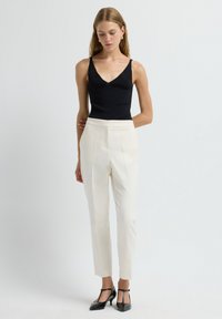 Black sleeveless top with a V-neck; cream tailored trousers; black dress shoes with T-straps; smooth textures and clean lines.