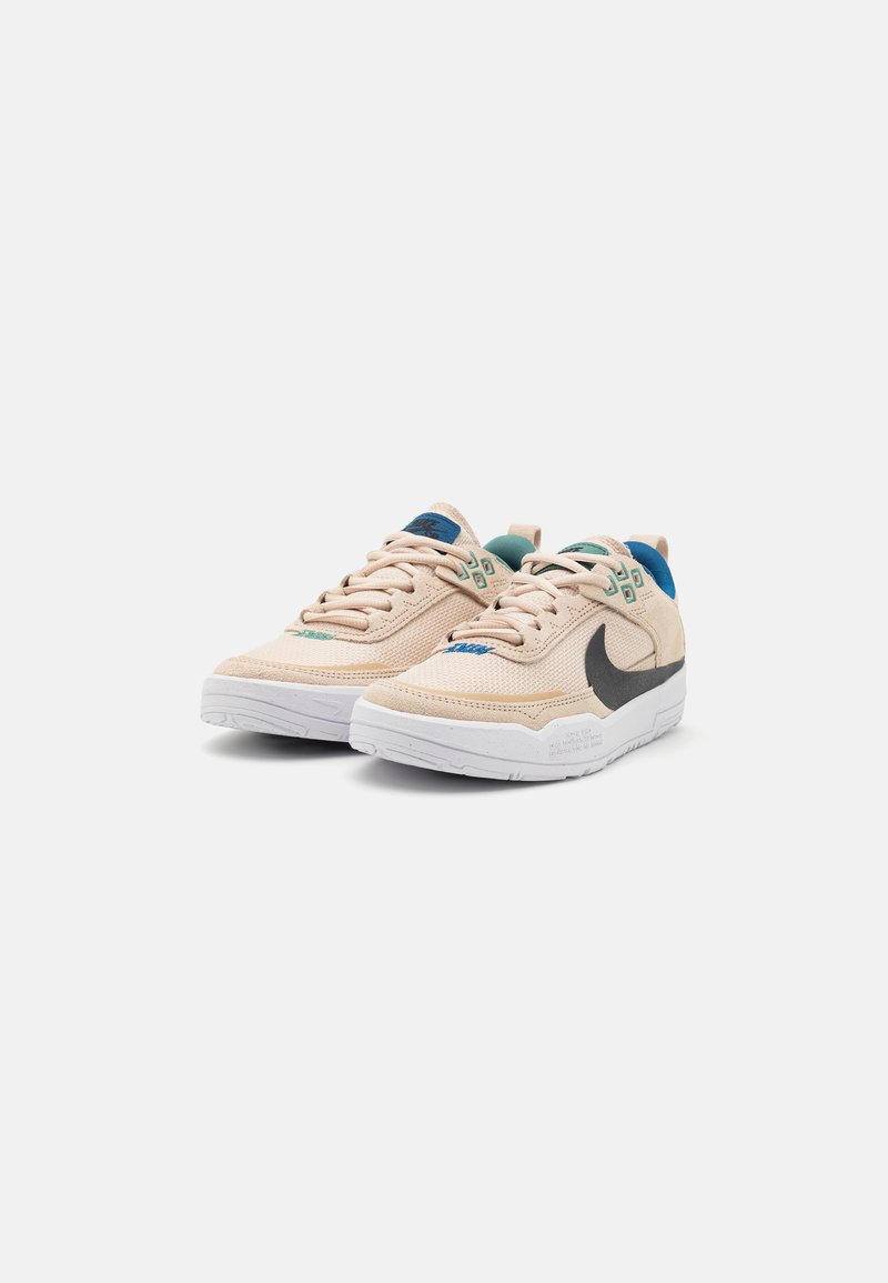 Beige textile-Sneaker mit strukturierter Oberfläche, schwarzem Swoosh-Logo, grünen und blauen Akzenten sowie einer weißen Gummisohle.