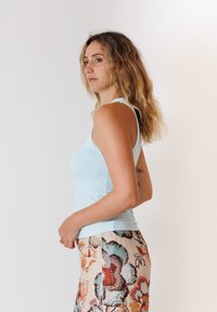 Canotta azzurro chiaro realizzata in tessuto elasticizzato, indossata con pantaloni a fantasia floreale che presentano tonalità di arancione, turchese e crema.