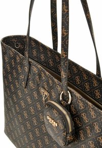 Sac fourre-tout noir avec motif logo beige, comprenant deux poignées, une poche zippée et une pochette ronde zippée amovible. Matériau texturé.
