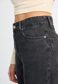 Čierne rifľové nohavice s vysokým pásom, hladkým povrchom, päťpokladovým dizajnom a kovovým zapínaním na prednej strane.