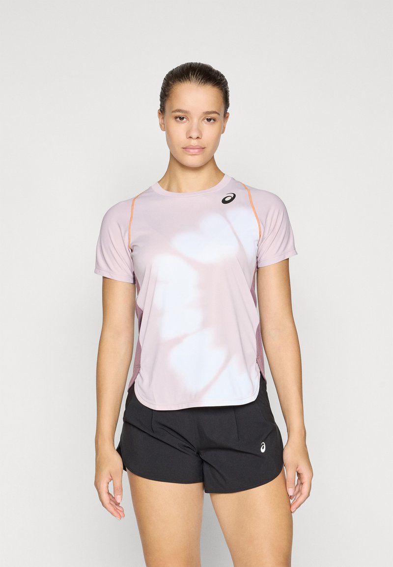 Helles rosa Sportshirt mit kurzen Ärmeln, einem runden Ausschnitt und orangefarbenen Akzenten; kombiniert mit schwarzen Shorts, die ein seitliches Logo aufweisen.