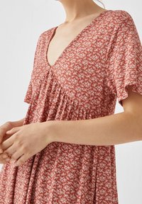 Rostfarbenes Kleid mit V-Ausschnitt, kurzen schwingenden Ärmeln und weißem Blumenmuster. Verfügt über geraffte Details unter der Brust und eine weiche Textur.
