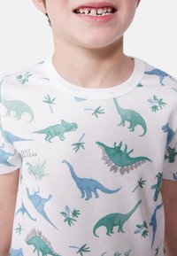 Biely bavlnený tričko s potlačou dinosaura v modrých a zelených odtieňoch, s rastlinnými motívmi. Krátke rukávy a okrúhly výstrih.