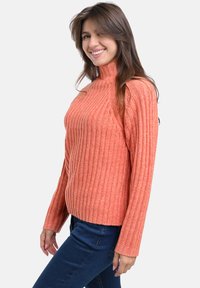 Rippstrick-Turtleneck-Pullover in hellorange, mit langen Ärmeln und einer figurbetonten Passform. Kombiniert mit blauen Jeans, die Textur und Farbkontrast zeigen.