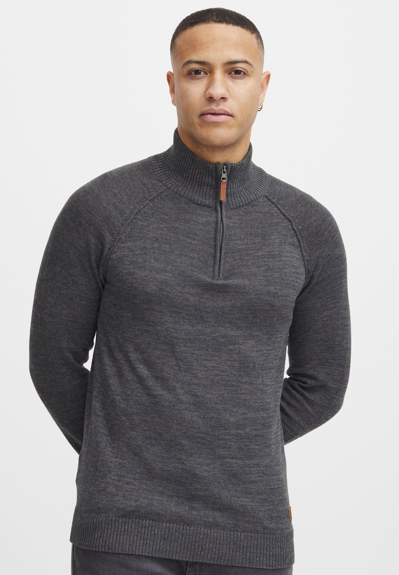 Maglione zip grigio scuro con colletto e polsini a coste. Presenta maniche raglan e una texture sottile. Accento in pelle vicino all'orlo.