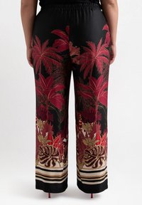 Black wide-leg pants with a vibrant floral pattern in red, gold, and green. Features an elastic waistband and striped hem detail.