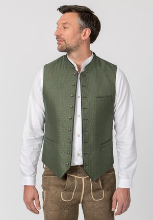 Mann in grüner gemusterter, geknöpfter Weste, weißem Hemd und brauner bestickter traditioneller Lederhose, der nach links schaut.