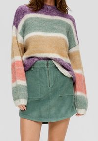 Suéter rayado multicolor en púrpura, verde y melocotón, combinado con una falda de pana texturada verde que cuenta con una cremallera frontal y bolsillos.
