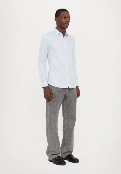 Cămașă albastră deschis cu mânecă lungă, închisă cu nasturi, asortată cu pantaloni gri texturați, având un croi lejer și pantofi negri. Design simplu și modern.