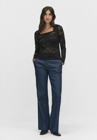 Zwarte kant lange mouwen top met een vierkante halslijn, gecombineerd met aansluitende donkerblauwe broek. De outfit heeft een soepele textuur en een op maat gemaakte uitstraling.