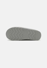Semelle de chaussure en caoutchouc grise avec un motif en zigzag texturé et une section centrale lisse. Talon arrondi et design avant effilé.