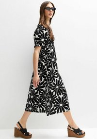 Zwart-wit bloemenprint jurk, korte mouwen,Gathered taille, midi-lengte. Gecombineerd met zwarte sleehakken, gladde textuur, gedurfde print.