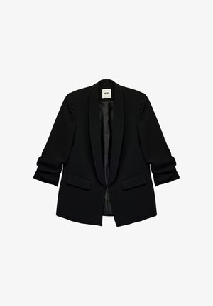 Blazer noir sur mesure avec col châle en satin, manches longues légèrement froncées, deux poches à rabat sur le devant et coupe ouverte.