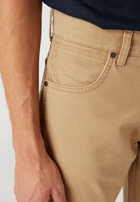 Pantalones de algodón beige con un diseño clásico de cinco bolsillos, costuras cosidas y herrajes metálicos con una textura suave.