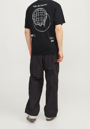 T-shirt en coton noir avec une impression graphique et un slogan au dos, associée à un pantalon cargo noir avec poches latérales et une coupe décontractée.