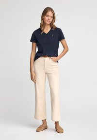 Marinblå V-ringad T-shirt i mjukt tyg, tillsammans med krämfärgade vida byxor, som har en minimalistisk design och lätt textur; brun skärp och skor.