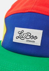 Wielokolorowa czapka z panelami w kolorze czerwonym, niebieskim, żółtym i zielonym. Zawiera białą metkę z napisem "Lil' Boo Copenhagen" w czarnym skrypcie.