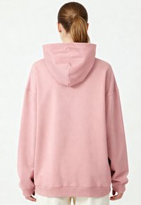 Sweatshirt rose surdimensionné avec une texture douce, poche kangourou et poignets côtelés, conçu avec une capuche à cordon et une coupe décontractée.