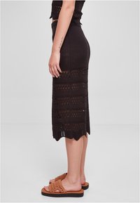 Strikket midi-skirt i mørkebrun med teksturert mønster og bølget kant, paret med lysebrune flettede sandaler for kontrast.