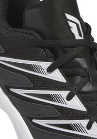 Svart atletisk sko med mesh-material, vita accenter och skarpt designade sidodetaljer. Har snörningar och en vadderad tunga för stöd.