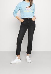 Jasnoniebieski, krótki sweatshirt z kwiatową grafiką i żółtym napisem, zestawiony z czarnymi spodniami o wysokim stanie i białymi sneakersami z czarnymi akcentami.