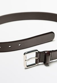 Donkerbruine leren riem met een glanzende zilveren rechthoekige gesp, plat gelegd op een witte achtergrond.