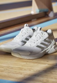 Hvide sneakers lavet af mesh og syntetiske materialer, med tre grå striber, teksturerede accenter og en holdbar gummisål.
