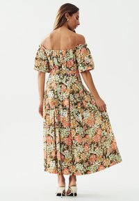 Bloemrijke maxi-jurk in groen, oranje en wit. Off-shoulder ontwerp met pofmouwen, elastische taille en vloeiende stof. Stiletto-hakken.