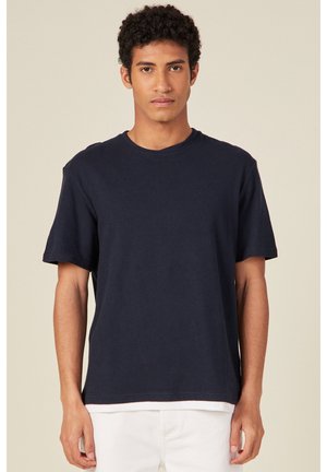 T-shirt in cotone blu navy con scollo rotondo, maniche corte e vestibilità rilassata, caratterizzato da una texture liscia e design minimale.