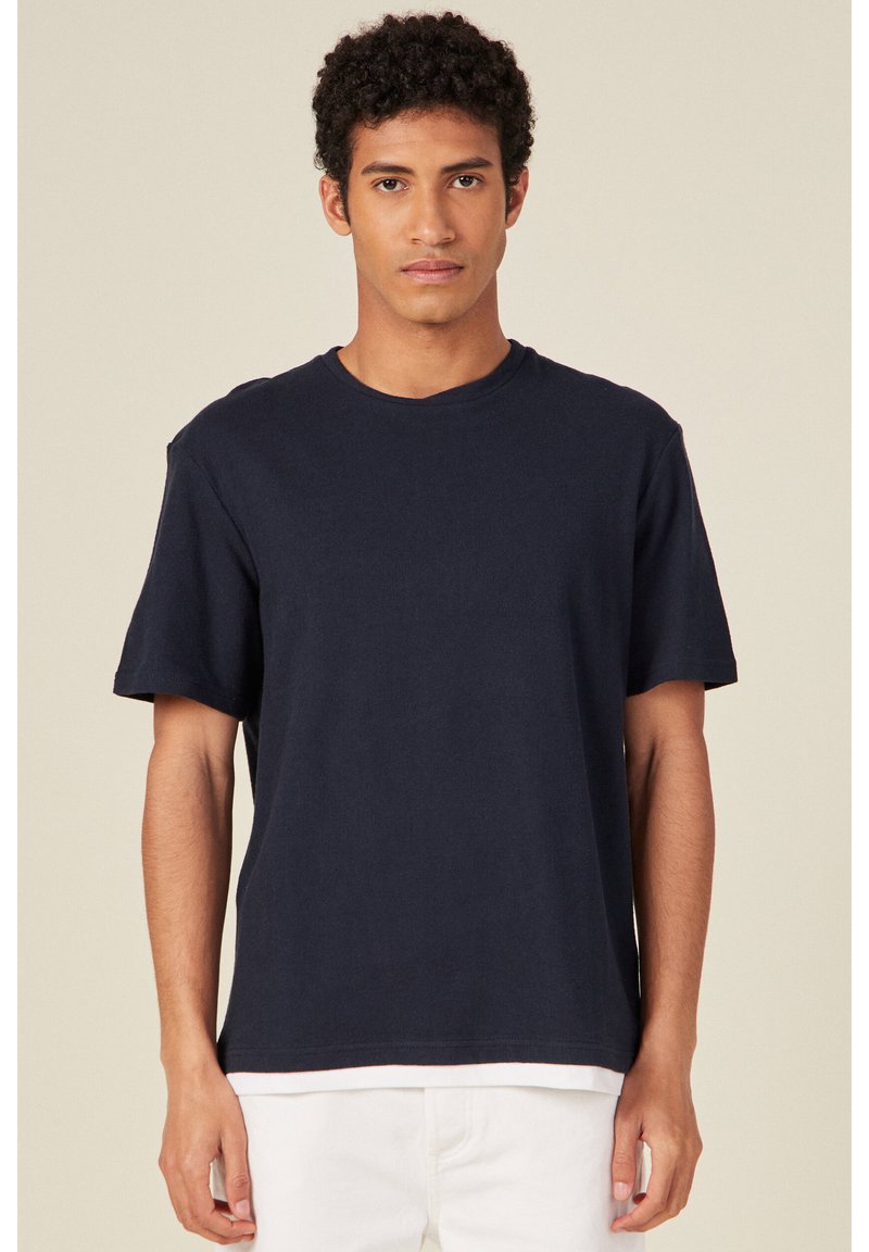 T-shirt in cotone blu navy con scollo rotondo, maniche corte e vestibilità rilassata, caratterizzato da una texture liscia e design minimale.