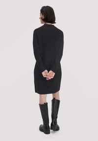 Strickkleid in dunkelblau, knielang, mit langen Ärmeln und strukturiertem Rippmuster, kombiniert mit schwarzen kniehohen Lederstiefeln.