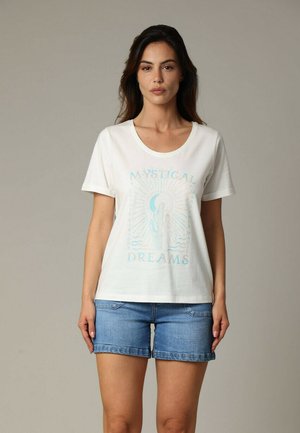 T-shirt en coton blanc avec impression graphique bleue arborant "RÊVES MYSTIQUE", col rond, manches courtes, associé à un short en jean.