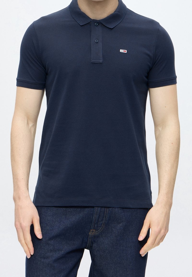Homme portant un polo bleu marine à manches courtes avec col et patte de boutonnage, associé à un jean bleu foncé.