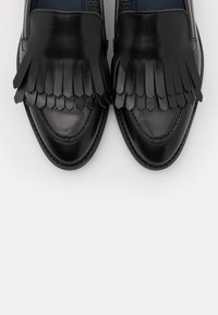 Mocassins en cuir noir avec un détail de franges décoratives à l'avant, une finition lisse et un bout rond avec des coutures contrastantes.