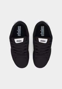 Ζευγάρι μαύρα αθλητικά παπούτσια Etnies με μαύρα κορδόνια και λευκές ετικέτες με το λογότυπο στην γλώσσα και τις φτέρνες, εμφανισμένα από πάνω σε λευκό φόντο.